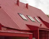 Rött, bandat plåttak med flera takfönster och skorstenar. Ett modernt hus med en slående takkonstruktion.