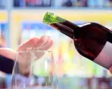 Hand stoppt Weinglas, während eine Flasche Rotwein eingegossen wird. Ein Symbol für bewussten Weinkonsum weltweit.