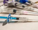 Flera sprutor med blå och lila detaljer ligger på en ljus yta. En spruta med blå kolv är i förgrunden, redo för vaccin i Colombia.