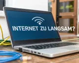 Laptop mit der Frage "INTERNET ZU LANGSAM?" und vielen Kabeln. Vielleicht liegt es daran, warum ist das Internet so langsam?
