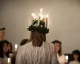En flicka med ljuskrona bär fram ett lucia namn. Hon leder en procession av flickor med ljus i mörkret.