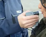 Policjant w mundurze z napisem "POLICJA" mierzy kobiecie poziom alkoholu alkomatem.
