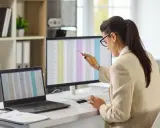 Kobieta w okularach pracuje przy komputerze, analizując dane finansowe. To typowe stanowisko w księgowości, gdzie liczy się precyzja i skupienie.