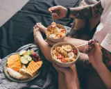 Para jedząca płatki z owocami i talerz świeżych owoców na łóżku. Zdrowy początek dnia, czyli zbilansowana dieta.