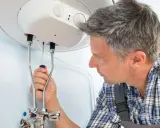Mann mit Werkzeug am Warmwasserspeicher. Anleitung zum Warmwasserspeicher entkalken.