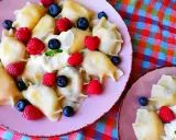 Pyszne pierogi z malinami i borówkami, polane śmietaną, na różowym talerzu. Letnia uczta pełna smaku.
