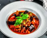 Un plat de ratatouille recette coloré et appétissant, garni de basilic frais, dans une assiette blanche.