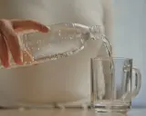 Dłoń przelewa wodę z butelki do szklanki. Szybkie nawodnienie organizmu to klucz do dobrego samopoczucia.