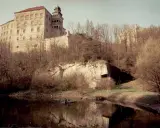 Zamek na skale nad wodą, otoczony drzewami. To krajobraz Ojcowskiego Parku Narodowego, najmniejszego parku narodowego w Polsce.
