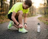 Ein Mann bindet sich die Schnürsenkel seiner Laufschuhe, bereit für eine Runde morgens oder abends joggen im Herbstwald.