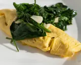 Złożony omlet francuski z zielonym szpinakiem i czosnkiem na białym talerzu.
