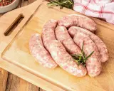 Surowe kiełbaski na desce, obok gałązka rozmarynu. Zastanawiasz się, jak długo można mrozić kiełbasę, by zachowała świeżość?