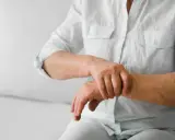 Osoba w białej koszuli masuje nadgarstek, odczuwając ból stawów rąk i nóg.