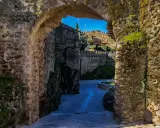Un arco de piedra revela un camino empedrado y murallas, evocando la atmósfera de pueblos medievales cerca de Madrid.