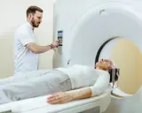 Pacjentka leży na stole do rezonansu magnetycznego, a technik obsługuje konsolę. Czy do rezonansu magnetycznego trzeba się rozebrać? Zazwyczaj tak, aby uniknąć zakłóceń.