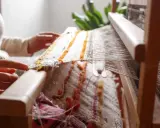 Hands weave a textured fabric on a loom, a beautiful example of textile upcycling.