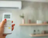 Mano con control remoto ajustando la temperatura ideal aire acondicionado para dormir a 25°C.