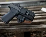 Pistolet w kaburze udowej z czarnego polimeru i brązowej skóry, z widocznym celownikiem optycznym.