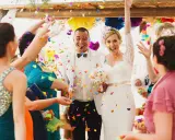 Glückliches Brautpaar im Konfettiregen, eine wunderschöne Tradition zur Hochzeit. Gäste werfen bunte Papierstreifen.