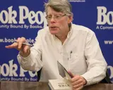 Stephen King, autore di libri da brivido, firma un volume. Sul tavolo, una bottiglia di root beer.