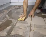 Man limpiando suelo porcelánico con una esponja. El suelo tiene un diseño de madera y un patrón curvo.