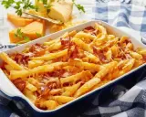 Zapiekane frytki z serem i chrupiącym boczkiem, podane w niebieskiej brytfance na kratkowanym obrusie.