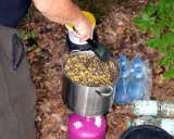 Przygotowanie grochu na ryby: duży garnek z ziarnami kukurydzy i grochu na kuchence turystycznej. W tle butelki z wodą.