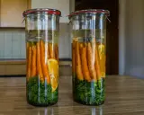 Zwei Gläser mit Karotten, Kräutern und Orangenscheiben in Salzlake zum Fermentieren.