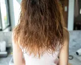 Wilgotne, brązowe włosy z widocznym **frizz** opadają na ramiona.