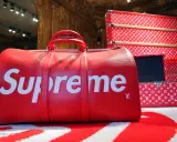 Czerwona torba podróżna z białym logo Supreme. Supreme to marka znana z limitowanych kolekcji i kolaboracji, jak ta z Louis Vuitton.