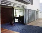 Una moderna casa con una contraventana corredera de lamas metálicas que protege un comedor interior.