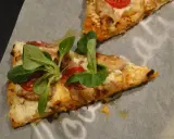 Dwie porcje pizzy z twarogu, z pomidorkami i świeżymi ziołami, na papierze do pieczenia.