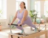 Frau lacht glücklich bei Pilates-Übungen auf einem Reformer. Pilates zum Abnehmen ist eine tolle Möglichkeit, fit zu werden.