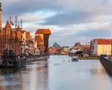 Gdańsk: zabytkowy żaglowiec cumuje przy Motławie, w tle Żuraw i nowoczesne budynki. Malowniczy opis miasta.