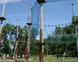 Śląski park linowy z drewnianymi słupami, siatkami i platformami na wysokości. Ludzie przygotowują się do zabawy.