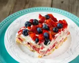 Tranche de tiramisu aux fruits rouges, garnie de fraises et myrtilles fraîches. Un délice estival.