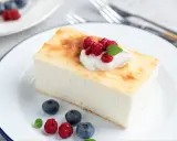 Pyszny sernik z dużej blachy, udekorowany bitą śmietaną, malinami i borówkami, na białym talerzu.