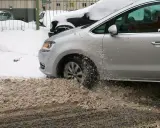Srebrny samochód próbuje wyjechać ze śniegu, koła mielą w błocie pośniegowym.