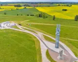 Pomnik i amfiteatr na polach grunwaldzkich, otoczone zielonymi łąkami i kwitnącymi polami rzepaku.