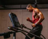 Schwitzender Mann im roten Tanktop läuft auf Laufband. Perfektes Cardio nach dem Krafttraining.