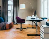 Accogliente stanza studio piccola con divano in pelle, scrivania regolabile, sedia viola e libreria a muro.