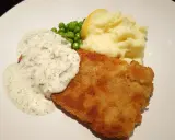 Panerad fisk med krämig kall sås till, serverad med potatismos, gröna ärtor och en citronklyfta.