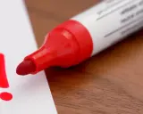 Roter Filzstift schreibt ein Ausrufezeichen auf weißes Papier. Ein wichtiger Hinweis, der sich leicht vom Filzstift von Haut entfernen lässt.