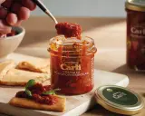 Une cuillère prélève de la crème de tomates séchées d'un pot Carli. Servie sur des crackers avec du basilic.
