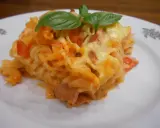 Pyszna zapiekanka z szynką, makaronem fusilli, pomidorami i ciągnącym się serem, ozdobiona listkami bazylii.