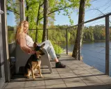 Relaks na tarasie z widokiem na jezioro. Kobieta głaszcze swojego psa, ciesząc się spokojem mazurskiej przyrody. Idealne mazury z psem.