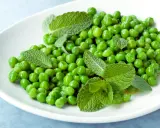 Petits pois frais et menthe sur une assiette blanche, une idée simple pour une recette de petit pois légère et savoureuse.
