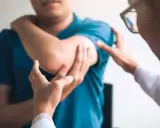 Un médecin examine le coude d'un patient, possiblement atteint du syndrome de la souris, une maladie professionnelle liée à l'usage intensif de l'ordinateur.