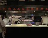 Chefs preparan cortes de carne en la parrilla Don Julio, con brasas ardientes y un ambiente de cocina profesional.