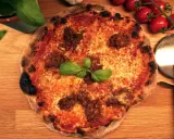 En napolitansk pizza med köttfärs som topping, garnerad med färsk basilika. Bredvid ligger en pizzaskärare och körsbärstomater.